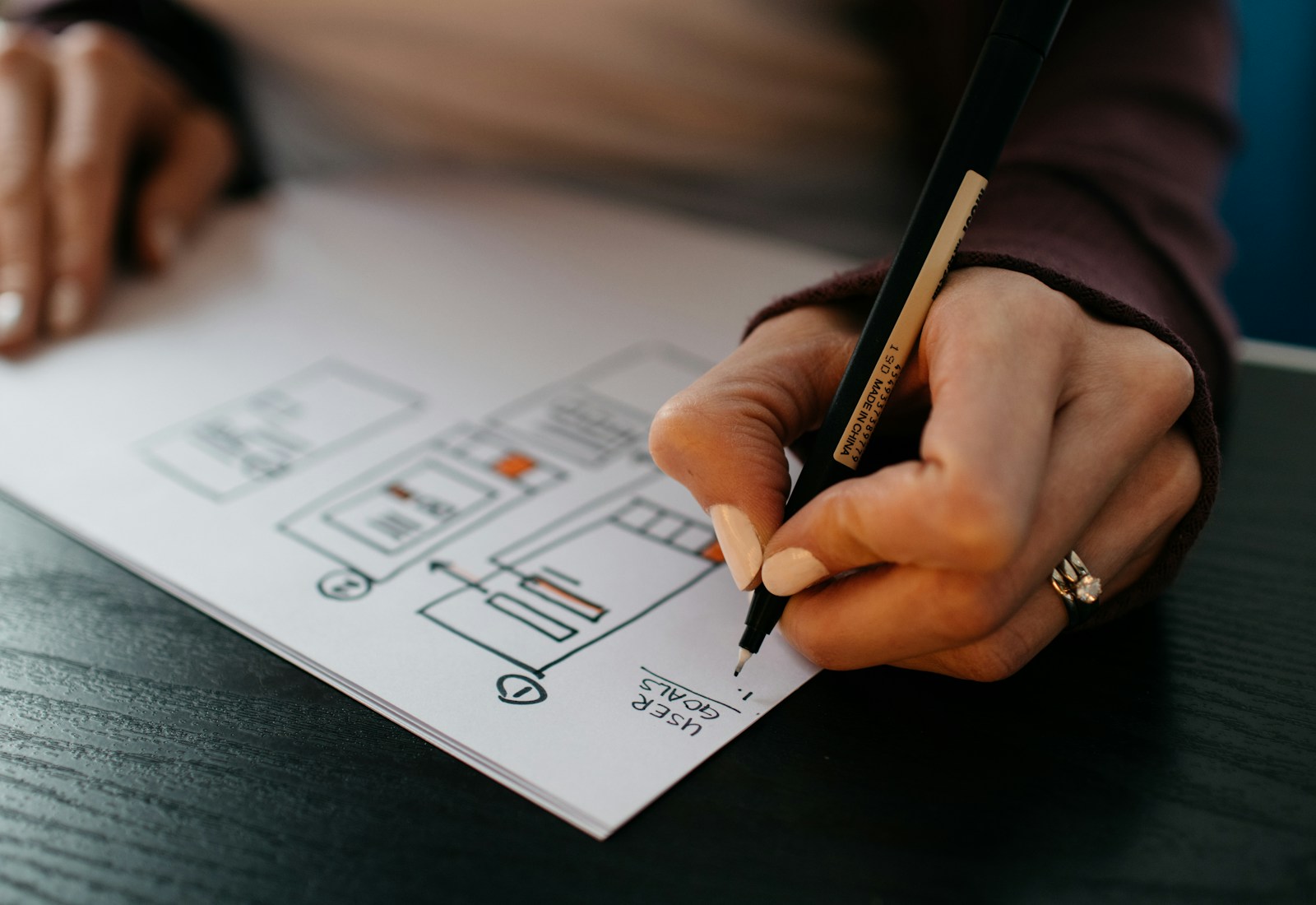 Hand sketching a user-interface wireframe with a fine pen on paper.